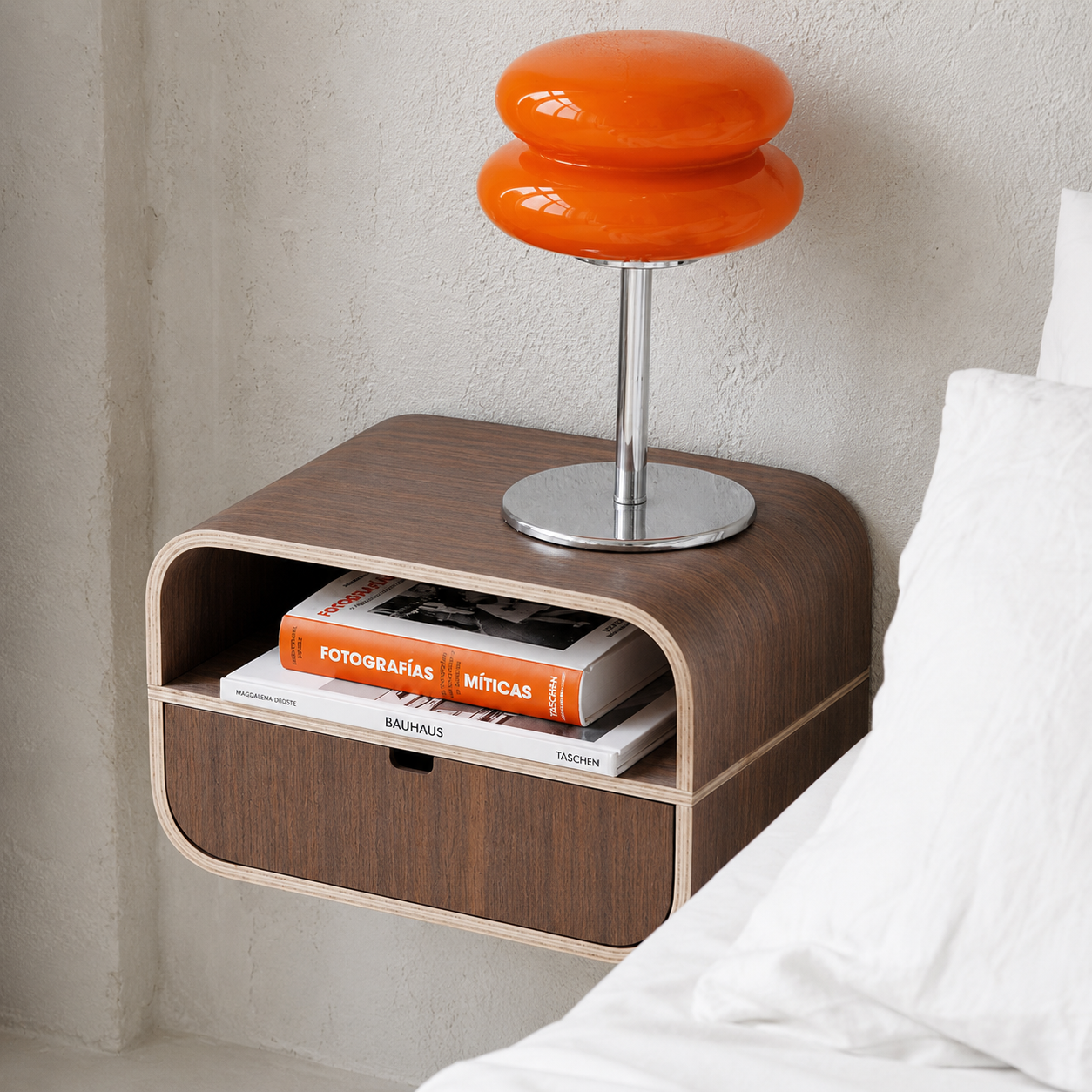 Modern wall-mounted bedside table with walnut veneer and open drawer holding books, styled in a minimalist room setting.