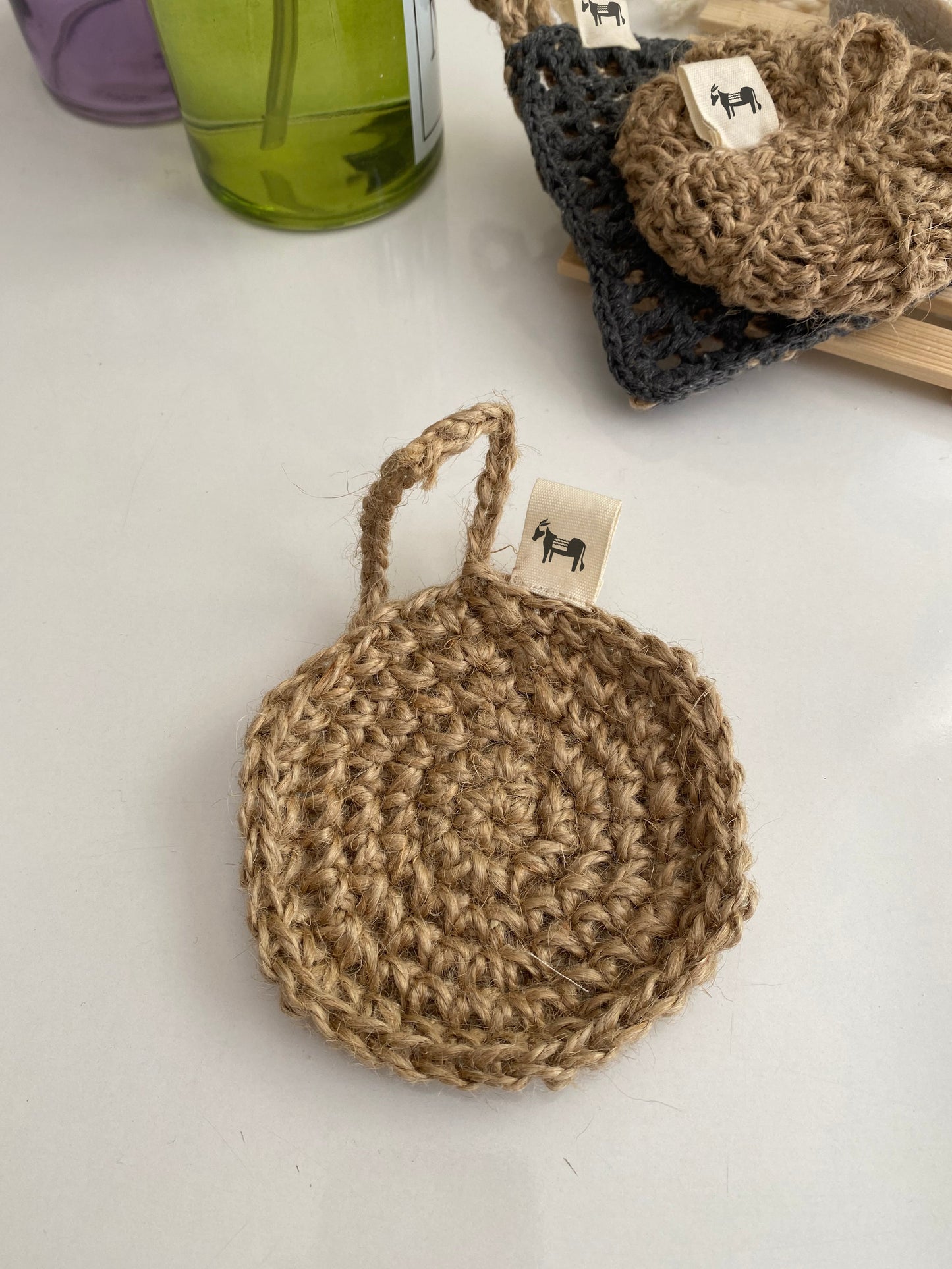 Jute scrubber 'Flat Earth' hanging on a hook, in a rustic bathroom setting.