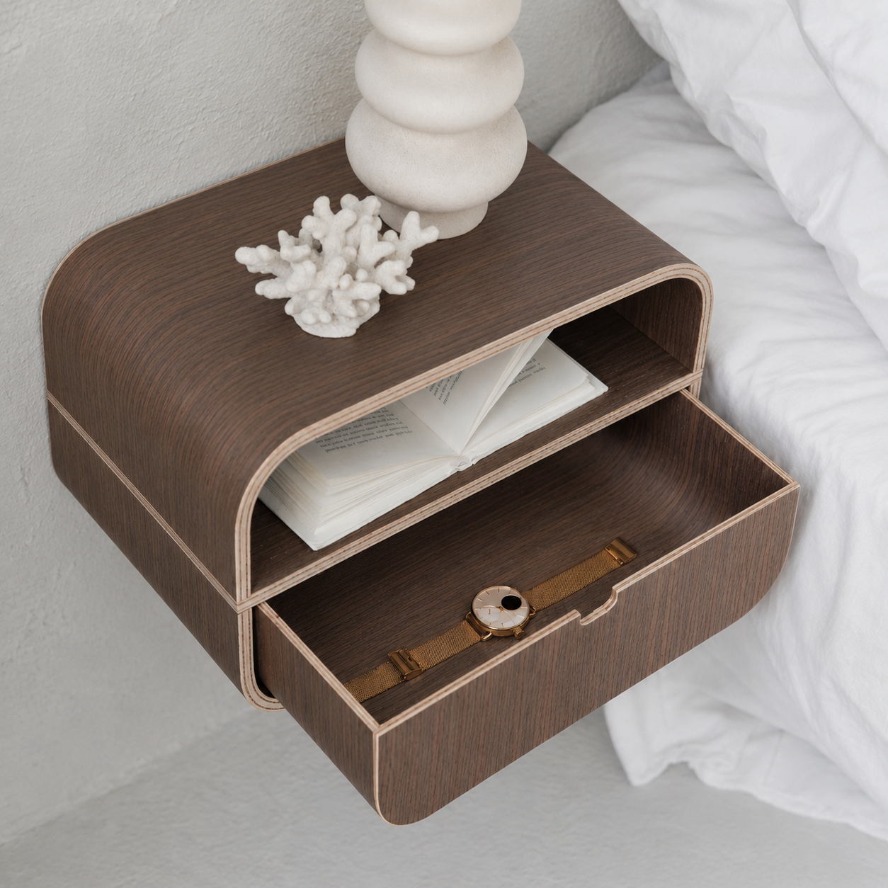 Minimalist wall-mounted nightstand with walnut veneer and open drawer containing a book, styled in a room setting.