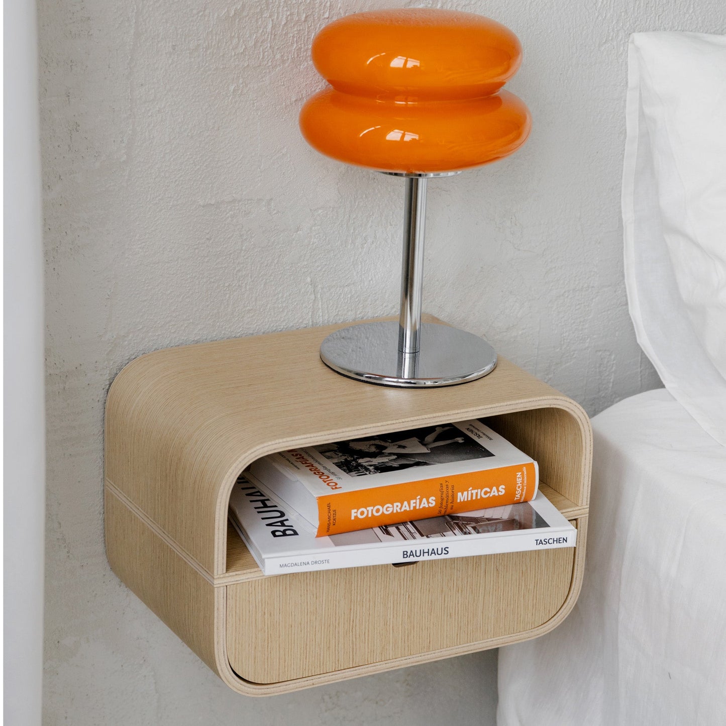 Modern wall-mounted bedside table with oak veneer and open drawer holding books, styled in a minimalist room setting.