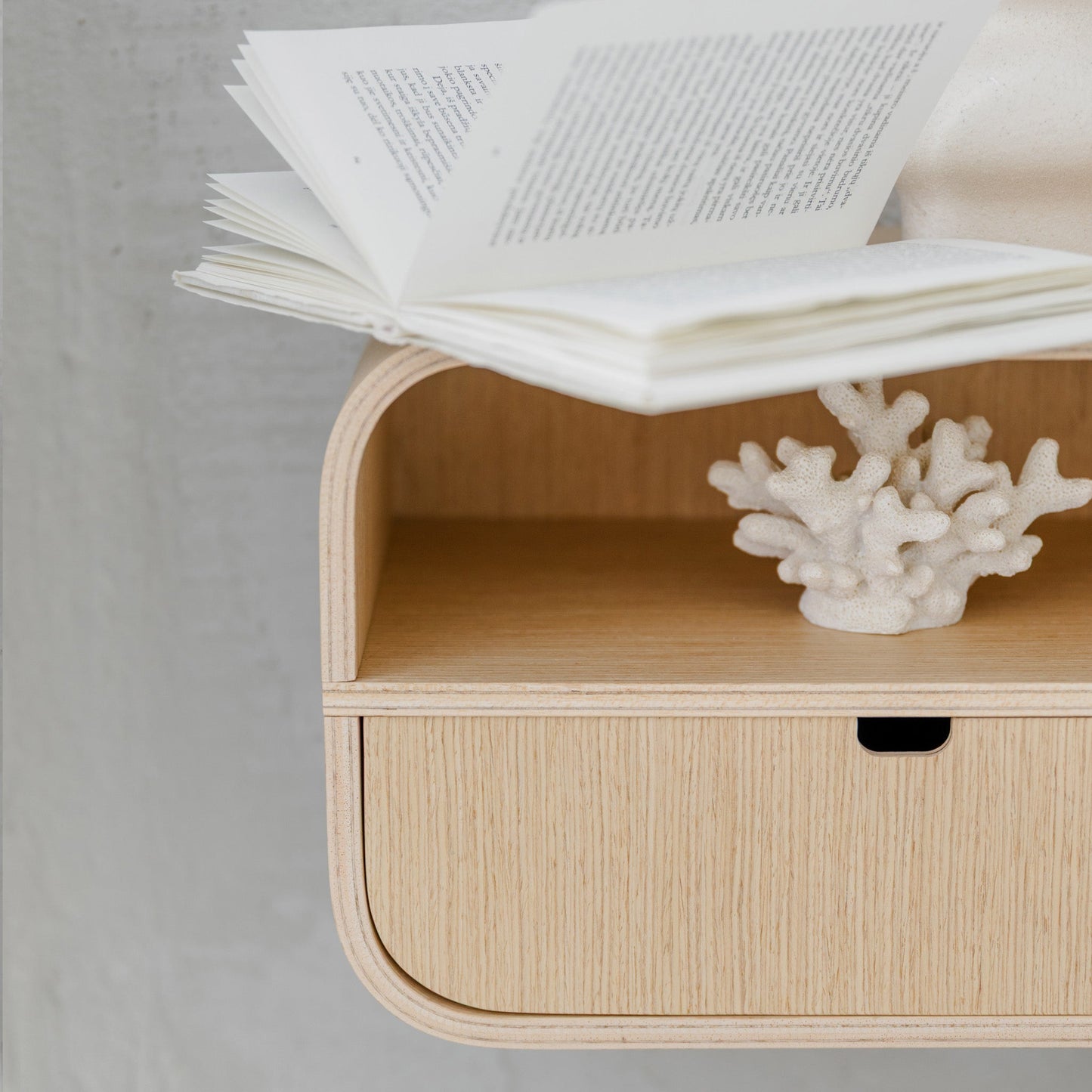 Minimalist wall-mounted nightstand with open drawer and coral decoration