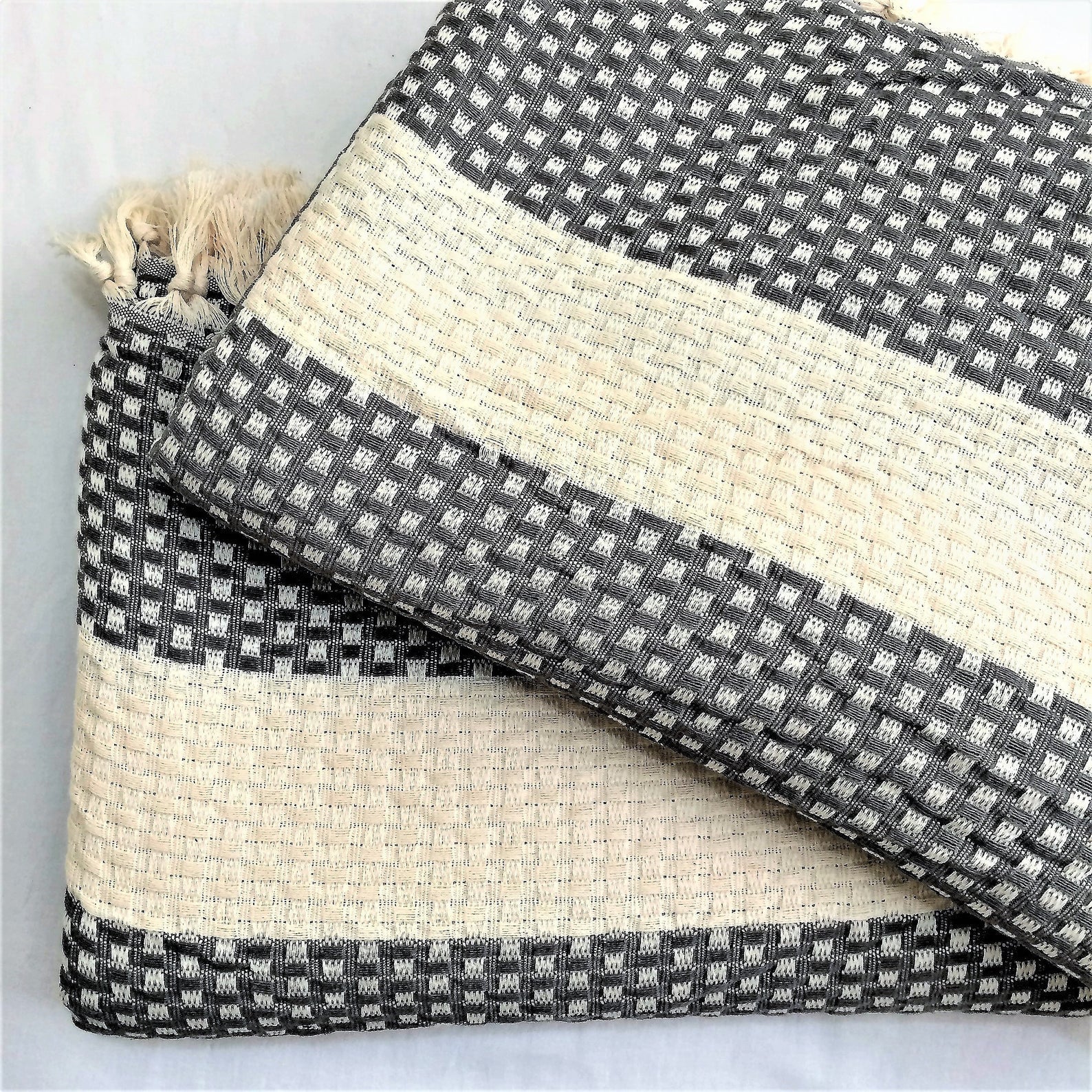 The Istanbul Handwoven Cotton blanket folded on a bed, with a few decorative pillows